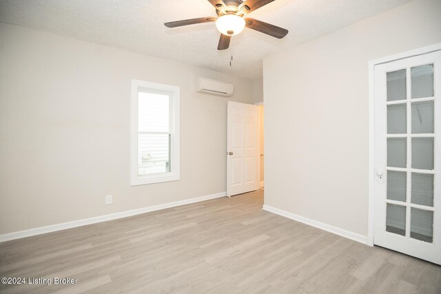 empty room featuring light wood finished floors, an AC wall unit, ceiling fan, a textured ceiling, and baseboards