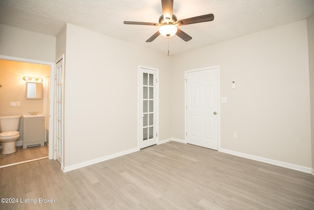 spare room featuring light wood-style floors, a ceiling fan, baseboards, and a textured ceiling