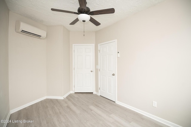 empty room with a textured ceiling, a wall mounted air conditioner, wood finished floors, and baseboards