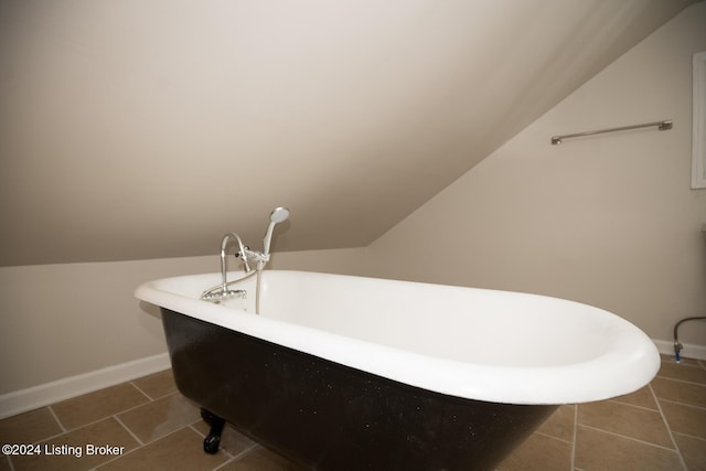 bathroom with lofted ceiling, a freestanding tub, baseboards, and tile patterned floors