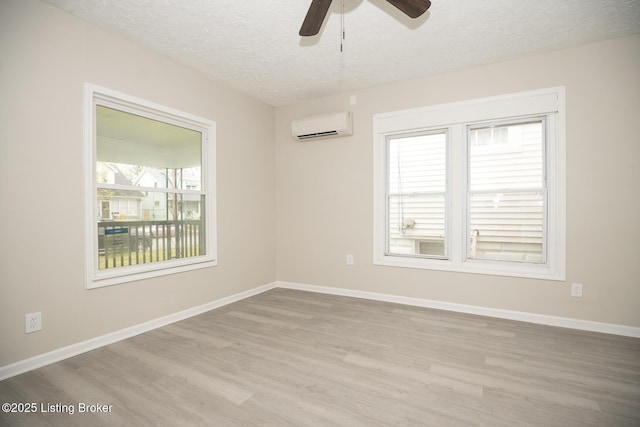 spare room with an AC wall unit, a textured ceiling, baseboards, and wood finished floors