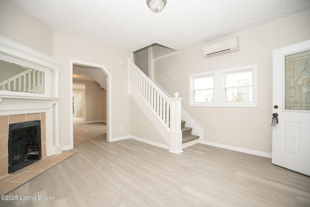 foyer featuring a wall mounted air conditioner, stairway, a tiled fireplace, and wood finished floors