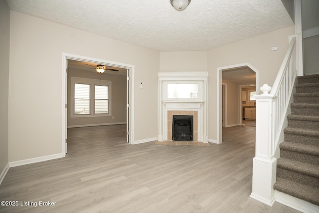 unfurnished living room with a textured ceiling, a tile fireplace, light wood-style flooring, baseboards, and stairway