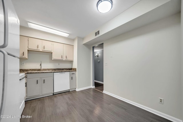 kitchen featuring white appliances, dark hardwood / wood-style floors, dark stone counters, and sink