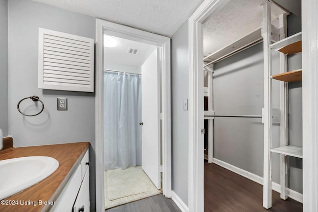 bathroom with a textured ceiling, vanity, walk in shower, and wood-type flooring