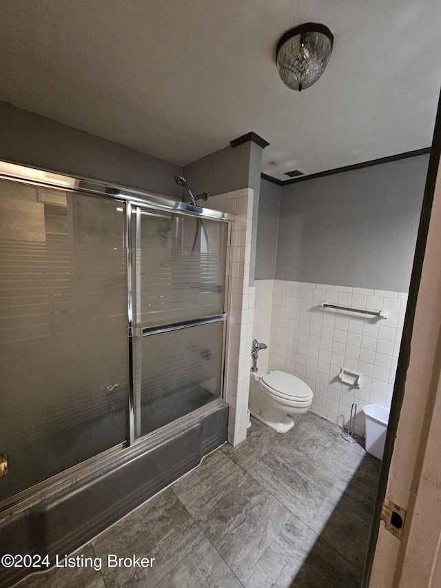 bathroom with a textured ceiling, toilet, enclosed tub / shower combo, and tile walls