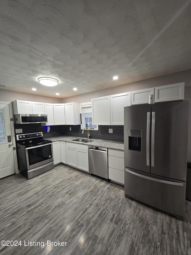 kitchen with appliances with stainless steel finishes, hardwood / wood-style flooring, and white cabinetry