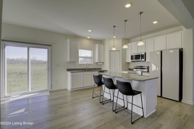 kitchen with light wood-type flooring, stainless steel appliances, decorative light fixtures, a center island, and white cabinetry