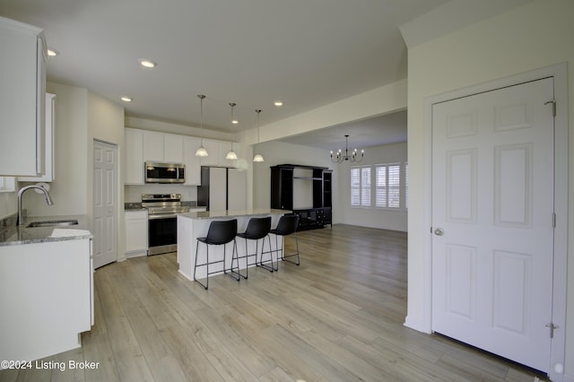 kitchen with appliances with stainless steel finishes, light wood-type flooring, sink, white cabinets, and a center island