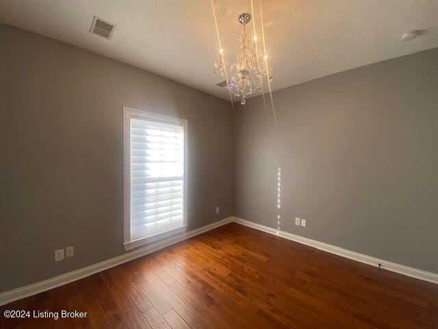 unfurnished room with a chandelier and dark wood-type flooring