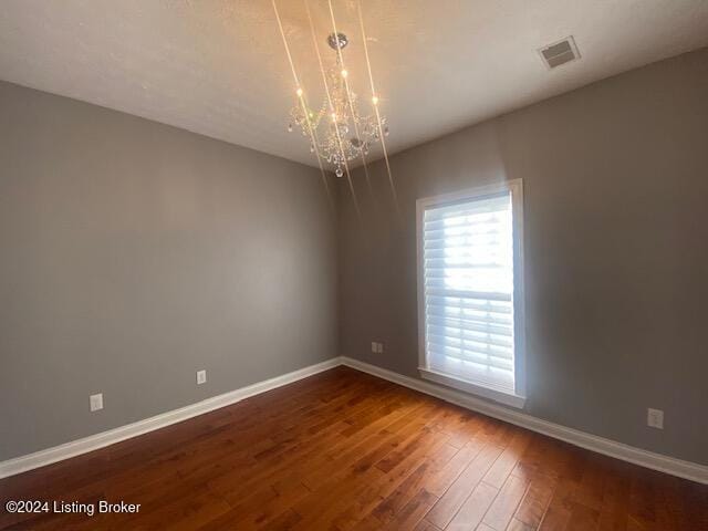 spare room with dark wood-type flooring and a chandelier