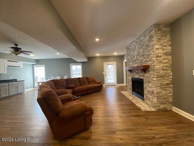 living room featuring an AC wall unit, ceiling fan, a fireplace, and wood-type flooring