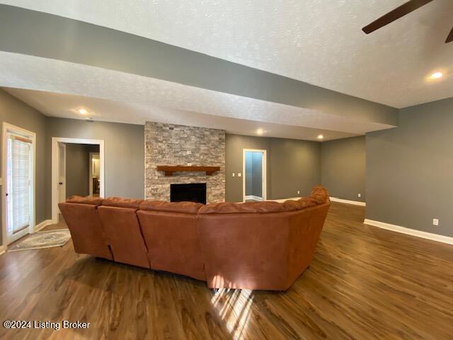 living room featuring a textured ceiling, dark hardwood / wood-style floors, a stone fireplace, and ceiling fan