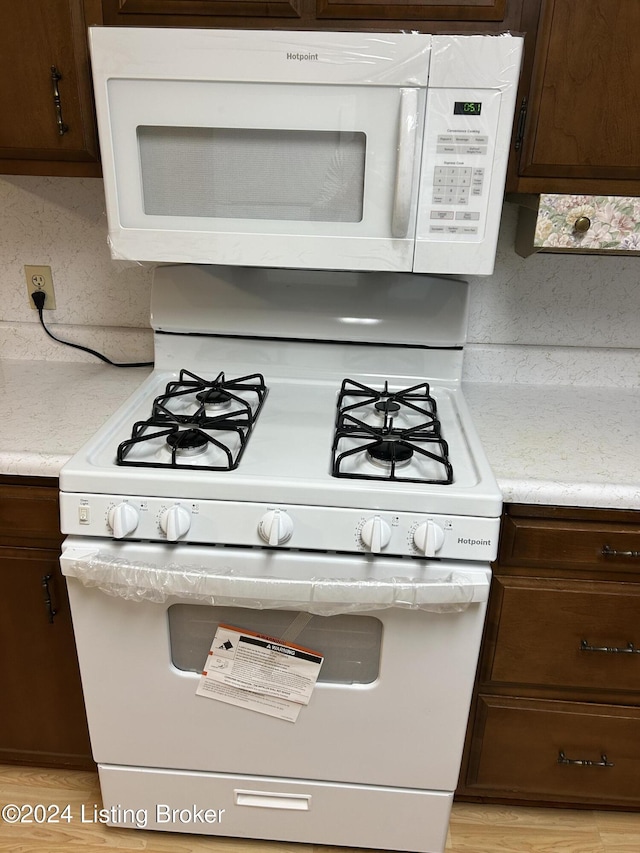 details featuring tasteful backsplash, dark brown cabinets, white appliances, and light wood-type flooring