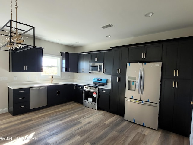 kitchen with stainless steel appliances, wood-type flooring, sink, and hanging light fixtures