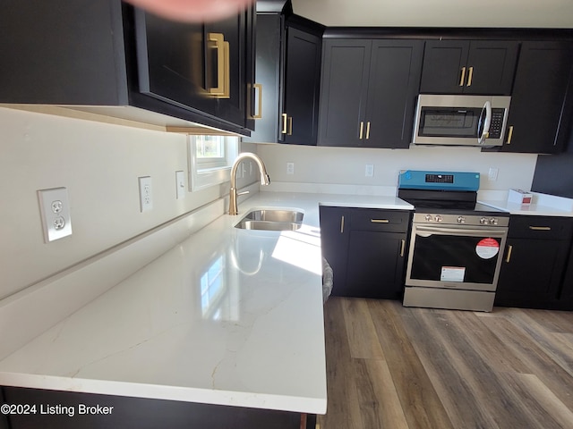 kitchen with light stone counters, stainless steel appliances, sink, and hardwood / wood-style floors