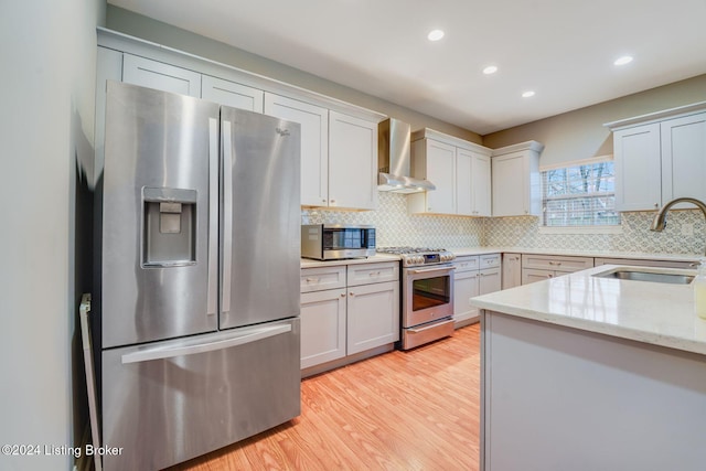 kitchen with white cabinets, wall chimney range hood, sink, light stone countertops, and appliances with stainless steel finishes