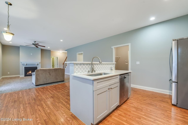 kitchen with a kitchen island with sink, sink, hanging light fixtures, light wood-type flooring, and stainless steel appliances