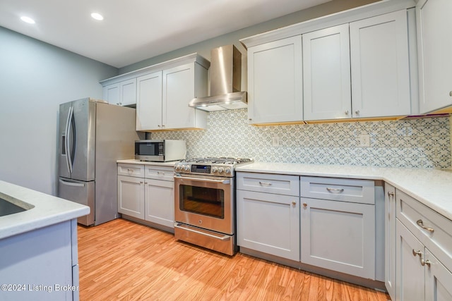 kitchen with decorative backsplash, stainless steel appliances, light hardwood / wood-style flooring, and wall chimney range hood