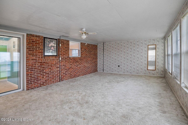 carpeted spare room featuring ceiling fan and brick wall