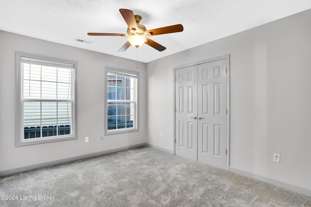 unfurnished bedroom featuring a textured ceiling, a closet, ceiling fan, and light colored carpet