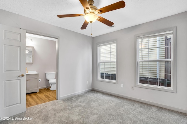 unfurnished bedroom featuring ensuite bathroom, ceiling fan, light carpet, and a textured ceiling