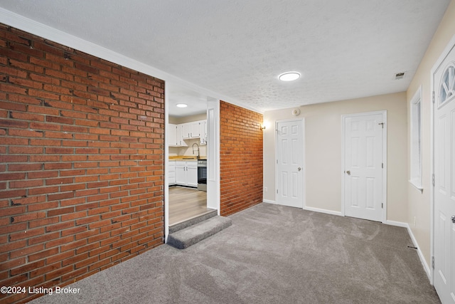 unfurnished living room with carpet floors, brick wall, and a textured ceiling