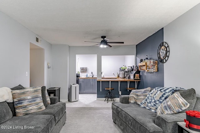 carpeted living room featuring ceiling fan, wet bar, and a textured ceiling