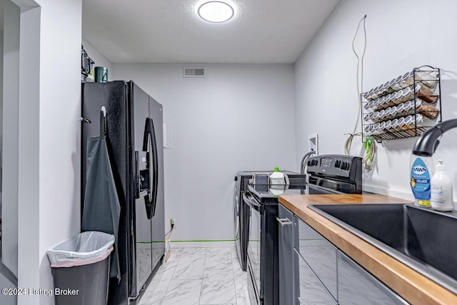 kitchen with butcher block countertops, sink, black appliances, and a textured ceiling