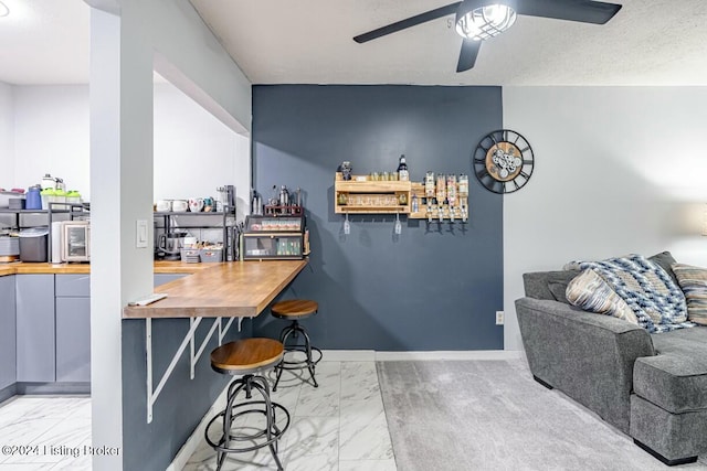 bar featuring ceiling fan, butcher block counters, and a textured ceiling