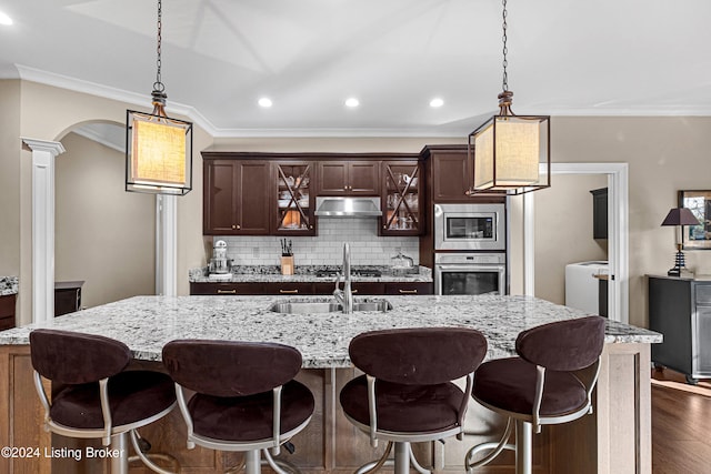 kitchen featuring ornate columns, sink, dark hardwood / wood-style floors, a center island with sink, and appliances with stainless steel finishes