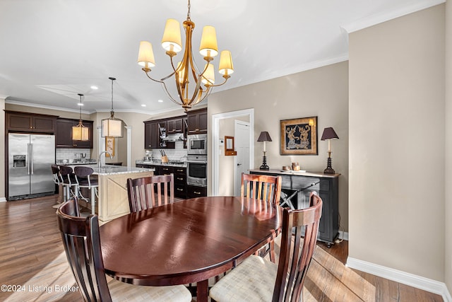 dining space featuring a chandelier, wood-type flooring, ornamental molding, and sink