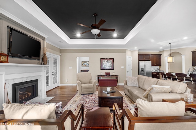 living room featuring ceiling fan, a raised ceiling, a premium fireplace, crown molding, and hardwood / wood-style floors