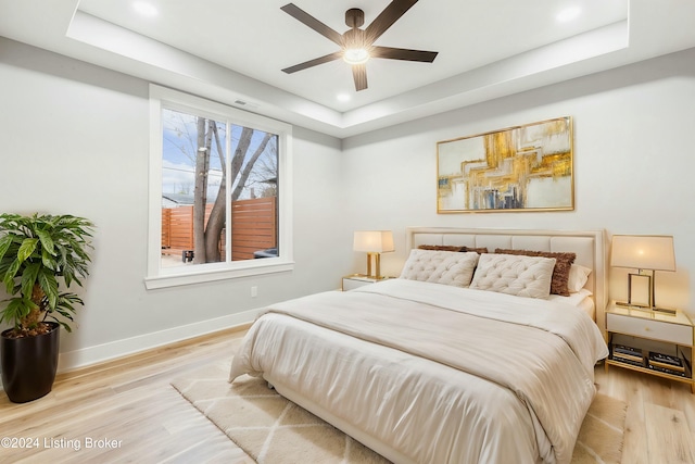 bedroom with ceiling fan, a raised ceiling, and light hardwood / wood-style flooring