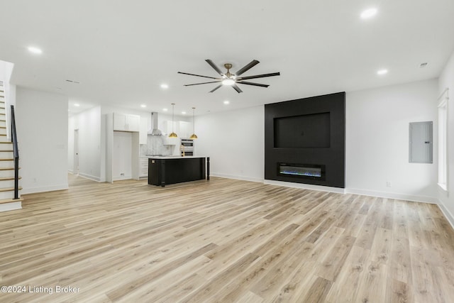 unfurnished living room featuring ceiling fan, light hardwood / wood-style floors, a fireplace, and electric panel