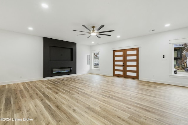 unfurnished living room with a large fireplace, ceiling fan, french doors, and light wood-type flooring