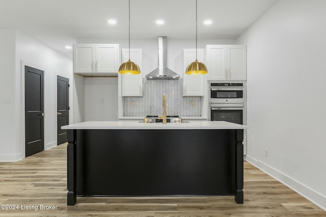 kitchen with white cabinets, a center island with sink, hanging light fixtures, and wall chimney range hood