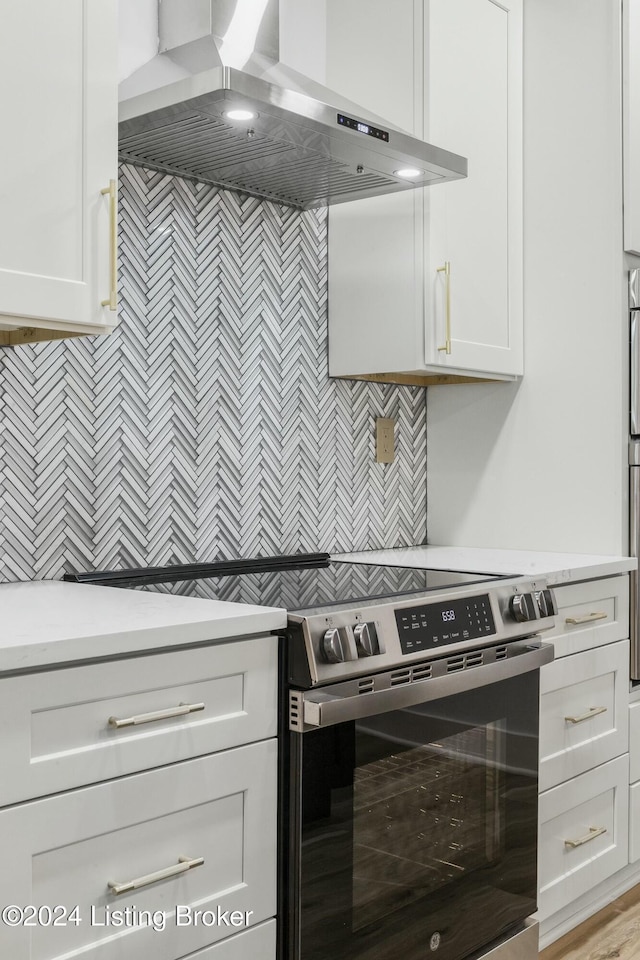 kitchen with light hardwood / wood-style floors, white cabinetry, stainless steel range with electric stovetop, and wall chimney range hood