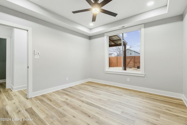 empty room with a raised ceiling, light hardwood / wood-style flooring, and ceiling fan