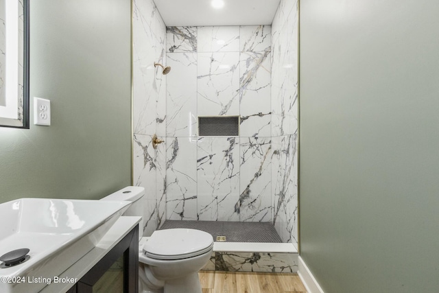 bathroom with hardwood / wood-style flooring, vanity, toilet, and a tile shower