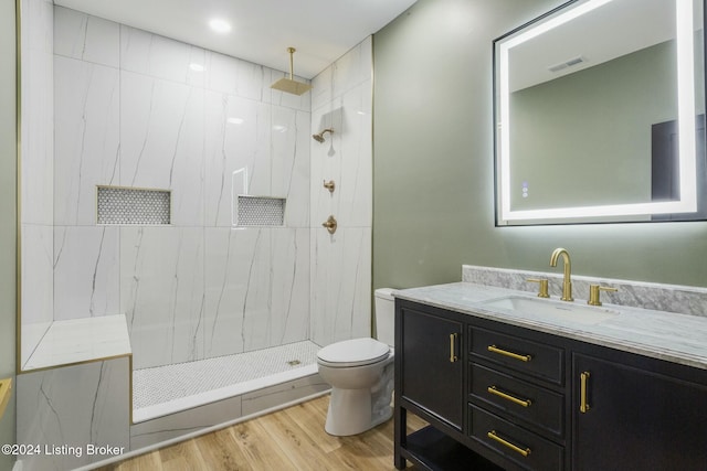 bathroom featuring hardwood / wood-style flooring, vanity, toilet, and tiled shower