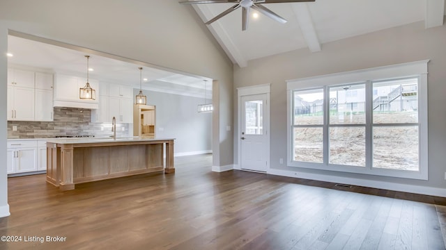 kitchen with a kitchen island with sink, white cabinets, hanging light fixtures, dark hardwood / wood-style floors, and beamed ceiling