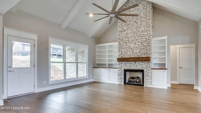 unfurnished living room featuring high vaulted ceiling, a stone fireplace, ceiling fan, light wood-type flooring, and beam ceiling