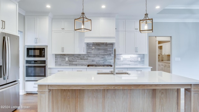 kitchen featuring stainless steel appliances, white cabinetry, hanging light fixtures, and a kitchen island with sink