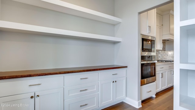 kitchen featuring white cabinets, wood-type flooring, stainless steel appliances, and tasteful backsplash