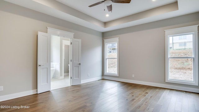 unfurnished bedroom featuring ensuite bath, hardwood / wood-style flooring, a raised ceiling, and ceiling fan