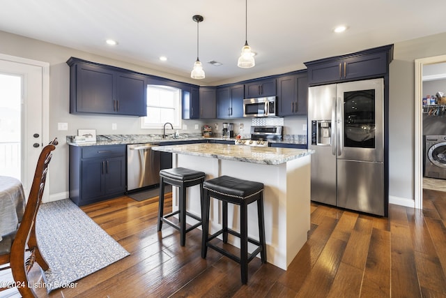 kitchen with sink, hanging light fixtures, dark wood-type flooring, stainless steel appliances, and a kitchen island