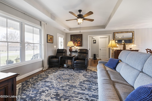 living room with dark hardwood / wood-style flooring, a raised ceiling, and ceiling fan