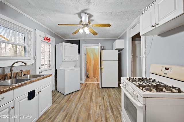 kitchen with white appliances, sink, light hardwood / wood-style floors, white cabinetry, and stacked washer / dryer