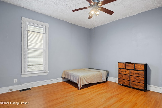 bedroom featuring a textured ceiling, ceiling fan, light hardwood / wood-style flooring, and multiple windows